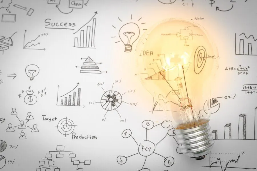 A glowing lightbulb surrounded by chalk drawings of charts and business ideas