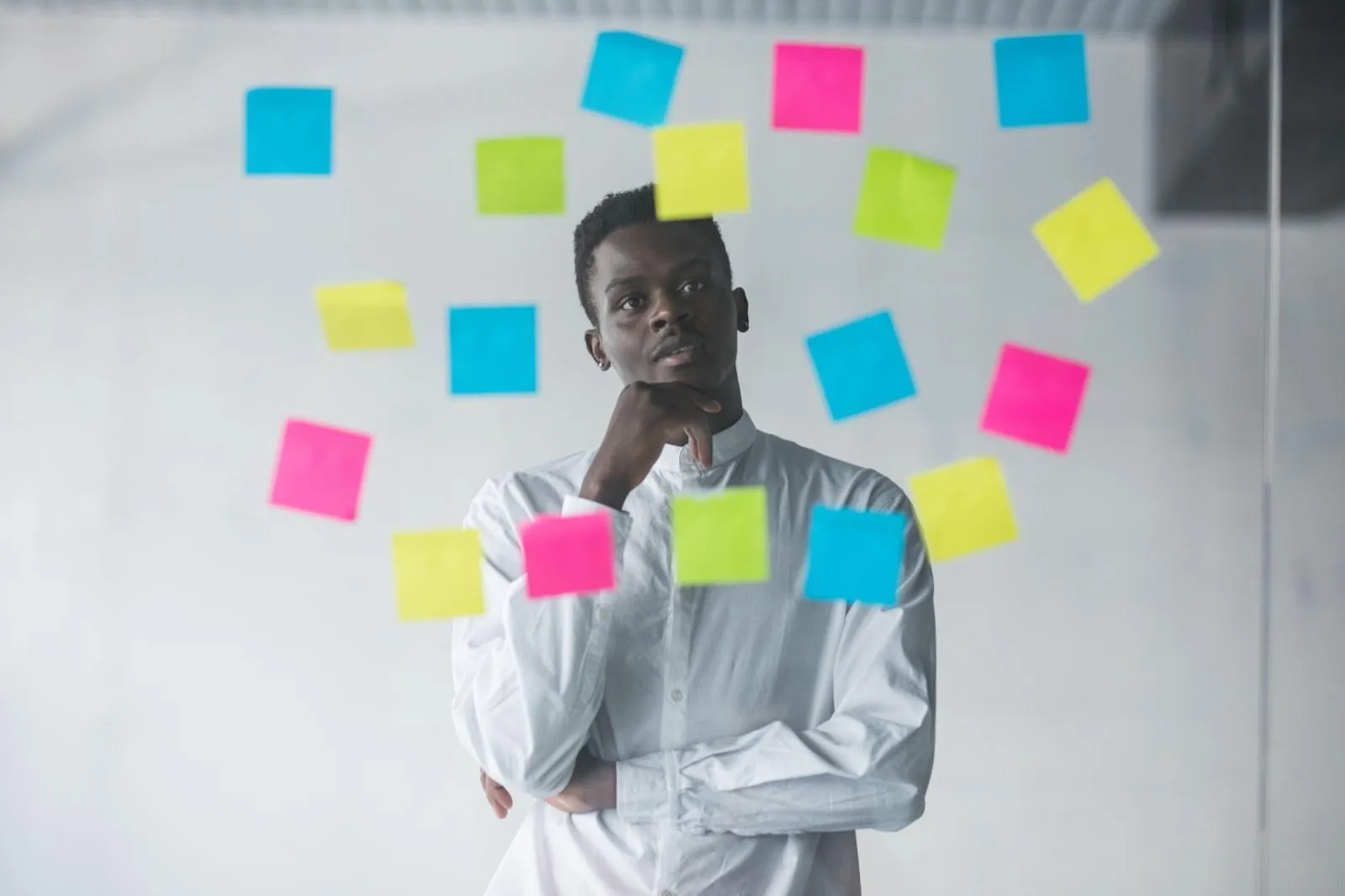 A man standing in front of a glass wall covered in coloured sticky notes