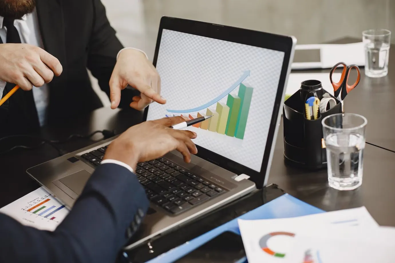 Two people pointing at a rising bar chart on a laptop screen
