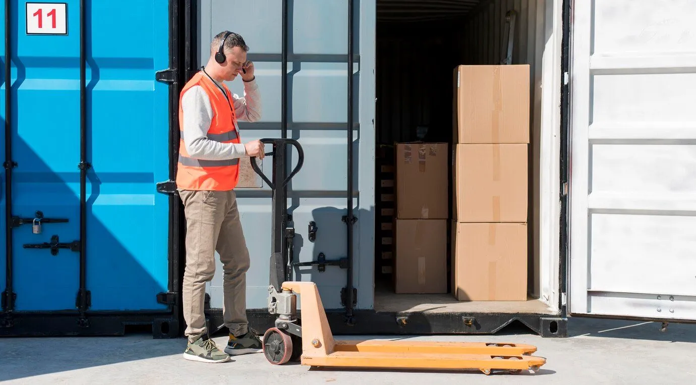 A worker in a hi-vis vest using a pallet truck to load boxes into a shipping container